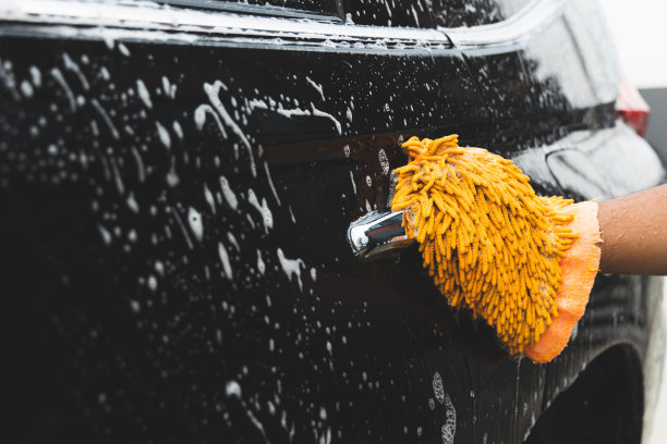 年轻人用泡沫清洗汽车。他戴着洗车用的手套。他擦了擦车身。图片下载