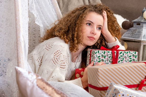 漂亮的年轻女人躺在圣诞礼品盒上穿白色针织套衫图片下载