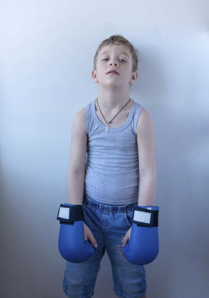 一个戴着蓝色拳击手套的可爱小男孩站在白色的背景上，在家训练，积极运动的生活方式图片下载