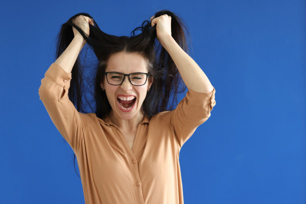 愤怒的女人戴着眼镜撕扯着蓝色背景的头发图片下载