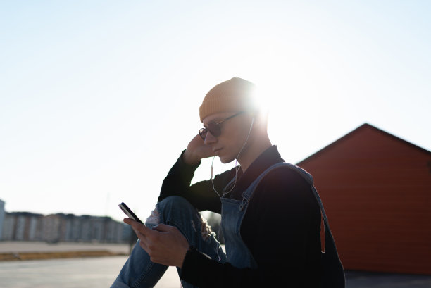 一名年轻男子坐在街上的长凳上使用智能手机图片下载