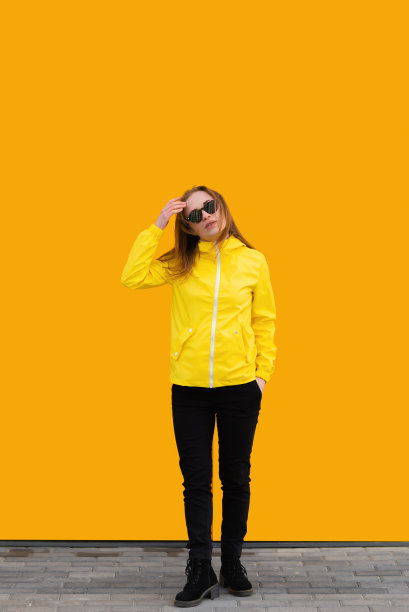 迷人的女孩固定她的头发在太阳眼镜和黄色雨衣孤立在黄色背景图片下载