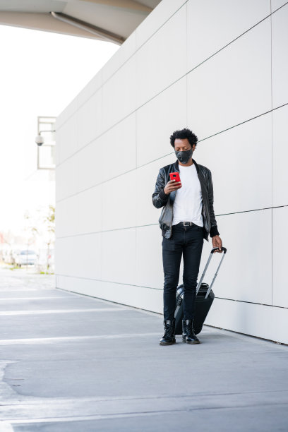 一名游客在户外使用手机和提着行李箱。图片下载