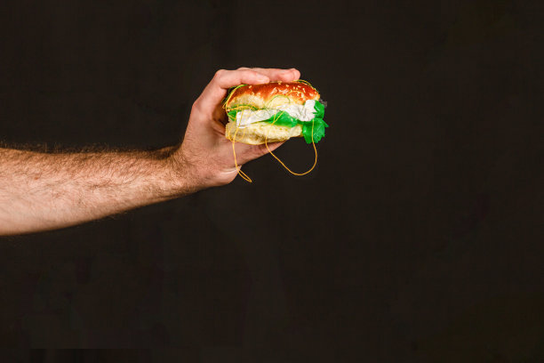 环境污染和食品工业。一个男人的手拿着一个塞满塑料和垃圾的汉堡包。黑色背景。本空间图片下载