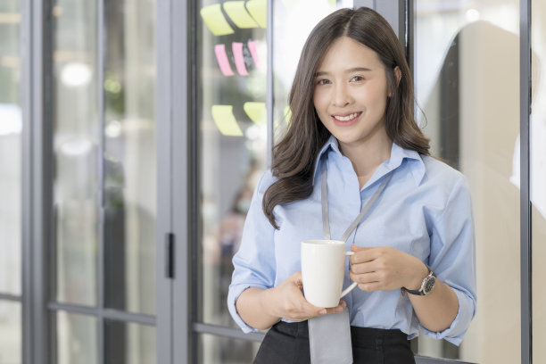 在办公室喝咖啡的年轻女商人。手捧热咖啡或茶图片下载