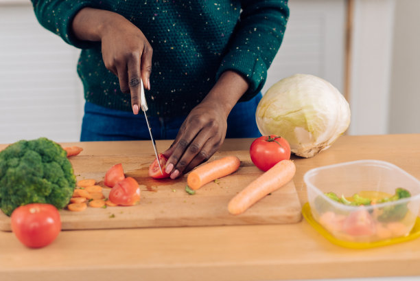 一位面目全的非裔美国妇女切蔬菜，然后装在塑料盒子里图片下载