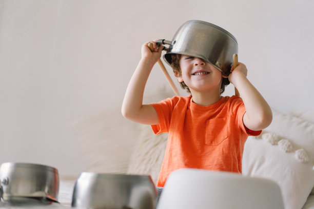 可爱的小男孩用木棍敲打摆得像鼓的炖锅。图片下载