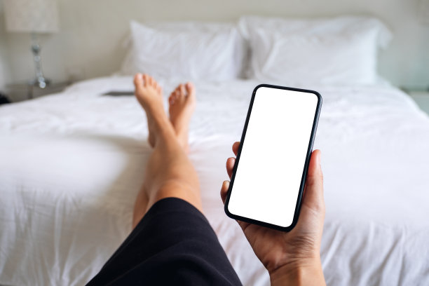 一名女子躺在床上放松时，拿着并使用手机，手机屏幕是空白的图片下载