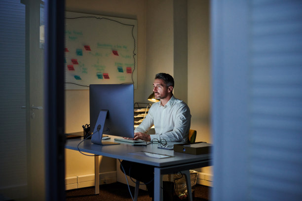 这是一个成熟的商人晚上在办公室用电脑工作的照片图片下载