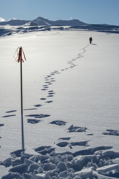 一艘探险游轮的工作人员将一面旗帜插在雪地上，向乘客展示路线，然后穿过一片平坦的白雪高原图片下载