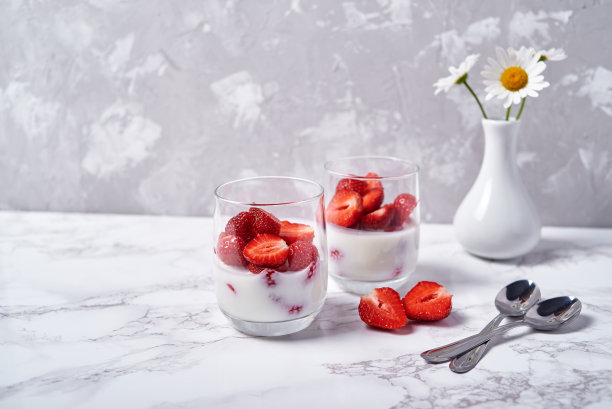 两杯健康的酸奶，新鲜的草莓切片，勺子和花瓶洋甘菊花，在白色的桌子背景，复制空间。健康早餐，食物理念图片下载