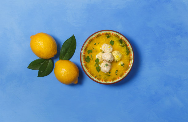 鸡汤加肉丸和柠檬汁。在蓝色的背景上，有两个柠檬，在中心，一个复制的空间图片下载