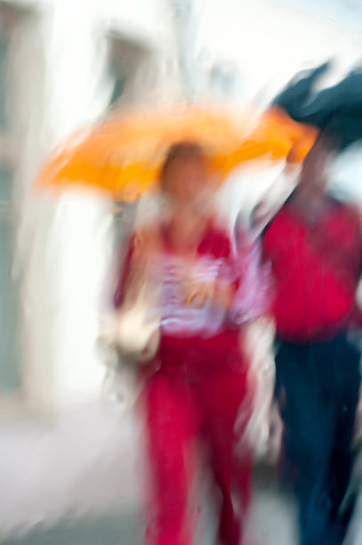 抽象的背景模糊了焦点，彩色的一对对男人和女人撑着雨伞在雨中穿过湿透的窗玻璃。印象主义风格。图片下载