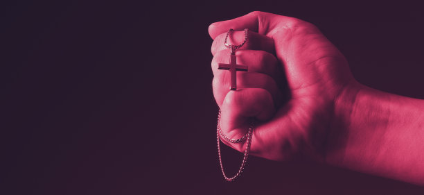 用念珠祈祷。天主教男子的手与念珠在黑色背景。手持耶稣基督的银念珠或十字架吊坠的双手。十字架和手在黑色背景。向神祷告的概念。图片下载