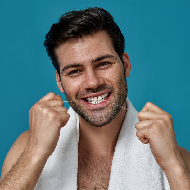 美丽的肖像快乐的黑发男孩看着相机，而清洁他的牙齿用牙线隔离在蓝色的背景图片下载