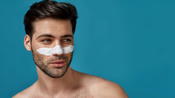 俏皮的黑发男子的肖像与白色面具应用在鼻子上清洁毛孔摆出孤立的蓝色背景图片下载