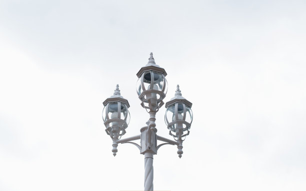 古老的路灯，映衬着白天明亮的天空。三盏灯挂在装饰柱子上。图片下载