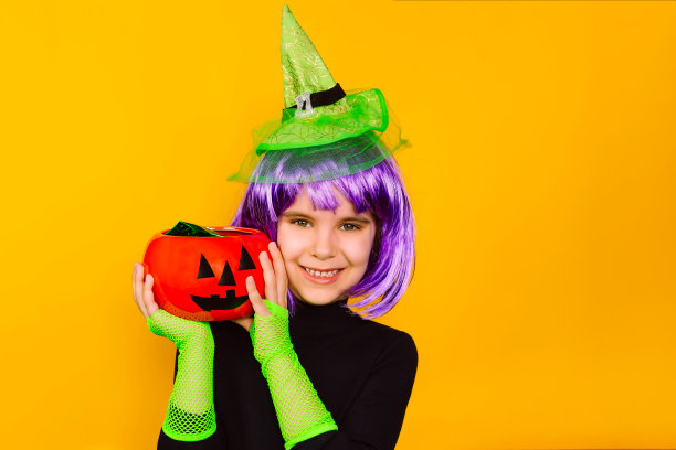 一个有趣的6岁小女孩穿着女巫服装，戴着一顶绿帽子，拿着一个南瓜脸的糖果碗。万圣节，传统，恐怖故事的概念。图片下载