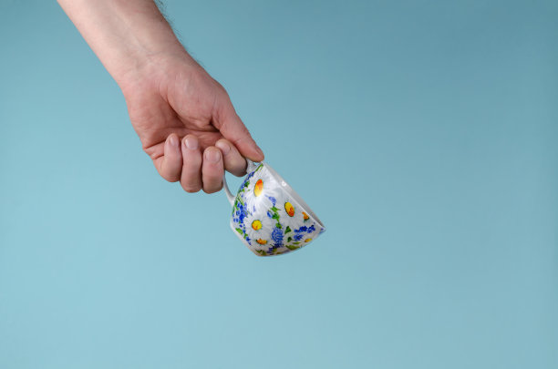 蓝色背景上的手和杯子。手持绘花白杯的男子。图片下载