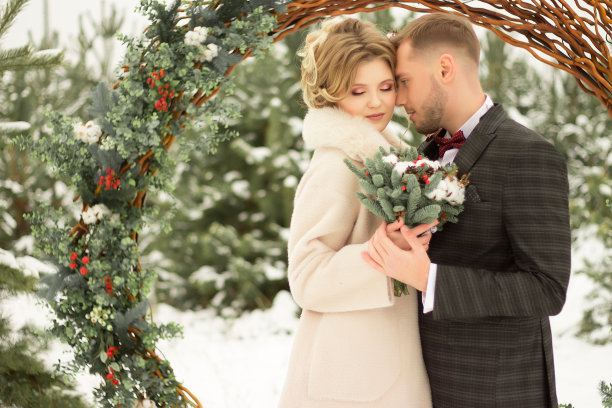 这对情侣拥抱着，亲吻着，手牵手，手里捧着一束花。有蝴蝶图案的套装，有裙子的外套。新娘和新郎图片下载