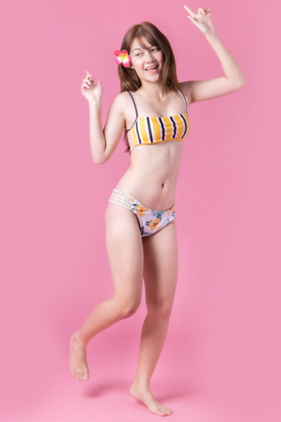 美丽，性感的亚洲女孩站在粉红色的背景。她穿着比基尼和微笑。暑假快乐旅行概念。混血女人听音乐。图片下载