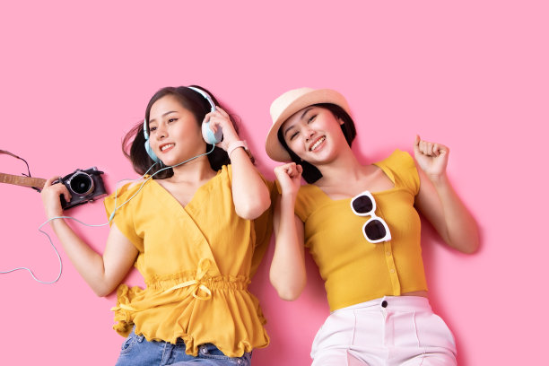 在粉红色的背景下，一个年轻的女人提着手提箱。漂亮可爱的梦幻女乘客的照片指着拷贝空间。图片下载