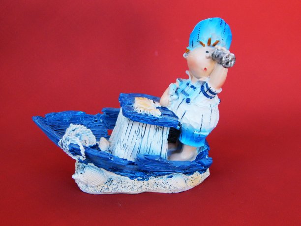 红色背景上小船上的小男孩雕像图片下载