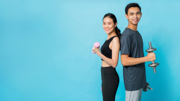 亚洲美丽快乐的女人拿着哑铃，和男朋友站在一起，在蓝色的背景上孤立地锻炼。概念苗条和健康的女孩锻炼。图片下载