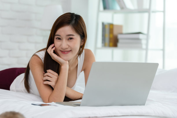 美丽迷人的亚洲年轻女子躺在床上，使用笔记本电脑使用社交媒体和网上购物放松在舒适的卧室在假期，生活方式在家里的概念图片下载