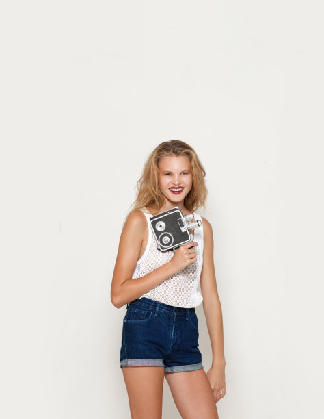 金发碧眼的女孩化着妆，手里拿着一台复古相机，看着相机，孤立的白色背景。图片下载