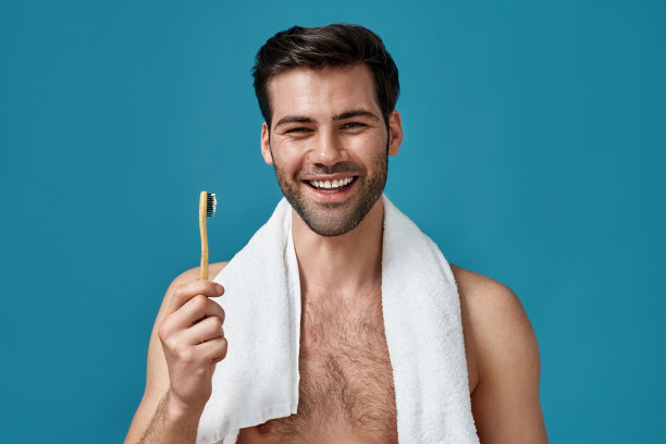 美丽的肖像快乐的家伙脖子上绕着毛巾对着相机微笑，拿着牙刷，在蓝色背景下摆出孤立的姿势图片下载