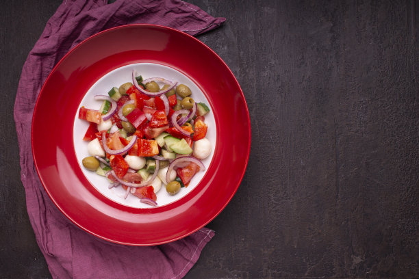 蔬菜沙拉，马苏里拉奶酪，橄榄油放在一个红色的盘子里，放在石头桌上。特写镜头。黑暗的照片。图片下载