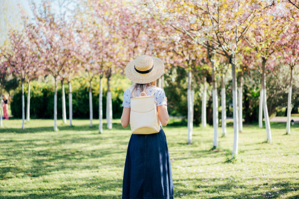 一个女人的后视图在一个春天的城市花园戴着一个背包的帽子。图片下载
