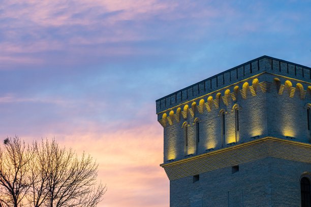 这座19世纪建筑的塔是用黄色砖块建造的，在落日的背景下被装饰性的黄色灯光照亮。图片下载