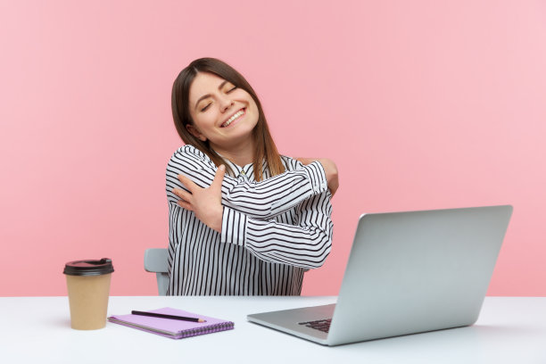 自私快乐的女上班族用快乐的表情拥抱自己，坐在工作场所，感到骄傲和满足图片下载