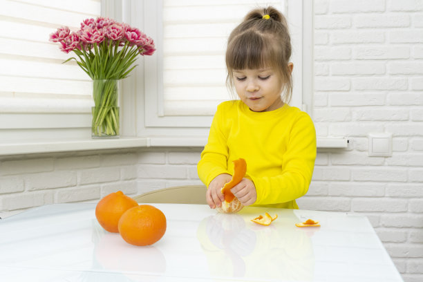 女孩在厨房的桌子上剥新鲜的橘子，特写图片下载