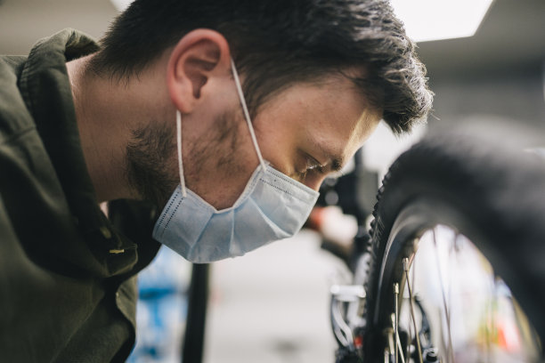 机修工戴着口罩在车间修理自行车。自行车店工作人员戴着防护口罩在隔离期间修理自行车。修理工维修周期。体育商店的概念图片下载