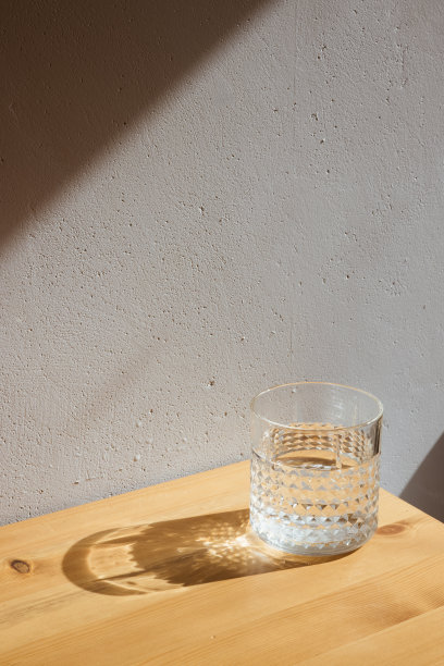 灰墙背景的木桌上，放着一只玻璃，清澈的水和清晰的影子图片下载