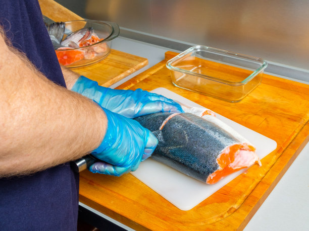 戴着卫生手套的厨师用刀切鲑鱼的身体。图片下载