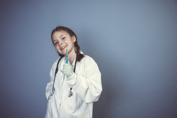 酷的年轻女孩打扮成女医生，带着听诊器和注射器在蓝色背景前摆姿势图片下载