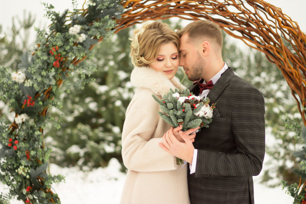 这对情侣拥抱着，亲吻着，手牵手，手里捧着一束花。有蝴蝶图案的套装，有裙子的外套。新娘和新郎图片下载