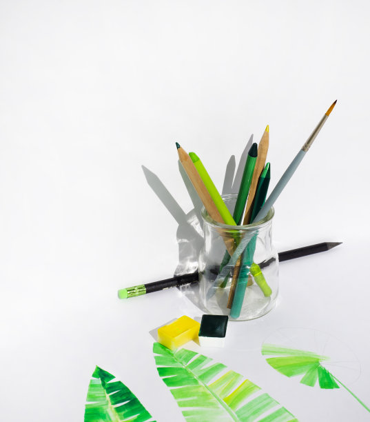 绿色的铅笔，玻璃瓶里的画笔和用来画绿叶的颜料。风格化的叶子是用水彩和彩色铅笔画的。白色背景作为拷贝空间。图片下载