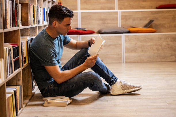 年轻的男学生在图书馆的书架上阅读和学习。阅读一本书。图片下载