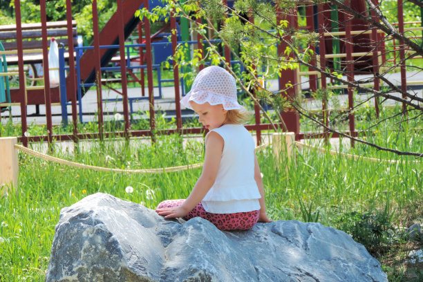 女孩坐在夏日公园的一块巨石上。图片下载