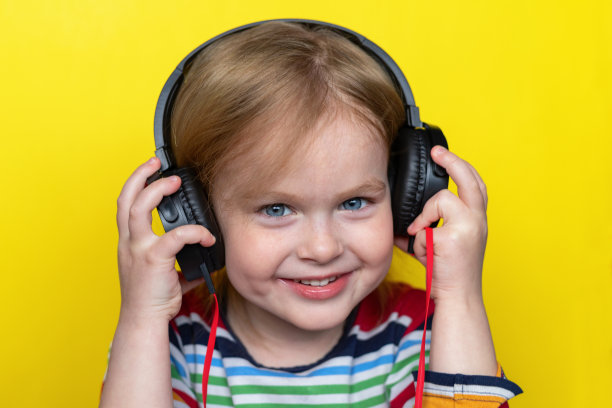 快乐的微笑的孩子听音乐与耳机在黄色的背景图片下载