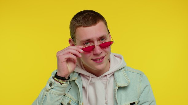 性感开朗的时尚男士穿着牛仔夹克戴着太阳镜，迷人的微笑在黄色的墙上图片下载