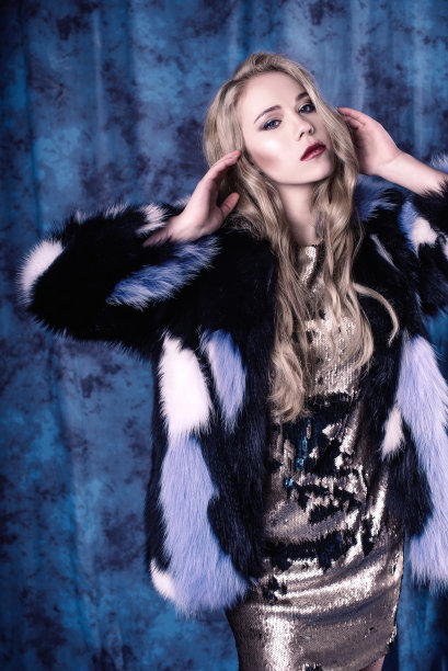 迷人的年轻女子摆姿势在亮片连衣裙和蓝色毛皮大衣。工作室的形象图片下载