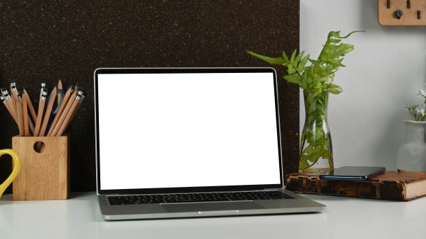 近景电脑笔记本电脑的空白屏幕，室内植物，笔筒和书的白色书桌。图片下载