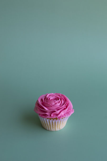 绿色背景上的玫瑰形状的美味纸杯蛋糕的垂直图像。礼物的概念图片下载