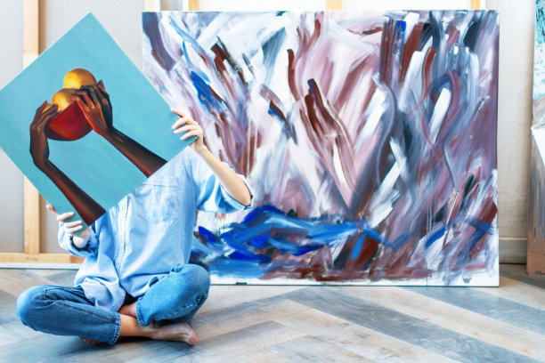 女艺术家坐在工作室的地板上，藏在一幅画后面图片下载